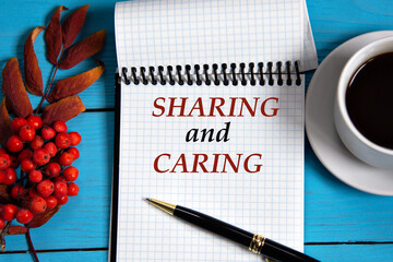 SHARING and CARING - words in a white notebook on a wooden blue background with a rowan branch and...