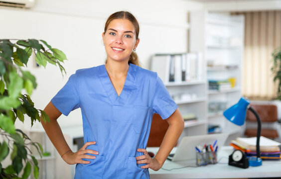 Portrait of successful confident young female doctor in blue uniform standing in modern medical office