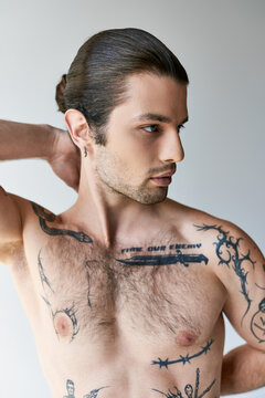 sexy good looking man with ponytail and tattoos in comfy underwear posing on ecru background