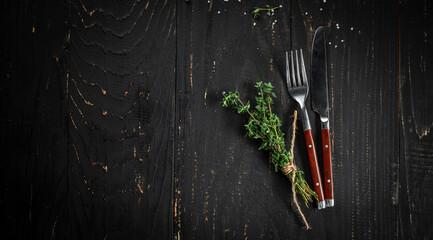 Knife and fork with bunch of fresh thyme on a dark background, Long banner format. top view. copy...