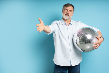Photo of positive old man hold disco ball isolated on blue background.