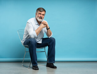 Portrait of a casual senior sitting on a chair on blue background