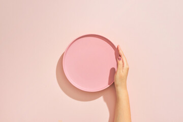 A female hands hold a empty(blank) pink dish(plate) on pink table(desk)