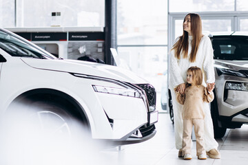 Mother with her little daughter choosing a car in a car showroom - obrazy, fototapety, plakaty