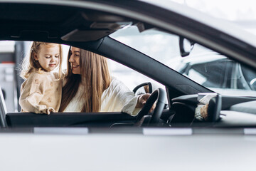 Mother with her little daughter choosing a car in a car showroom