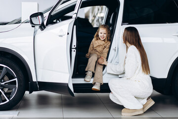 Mother with her little daughter choosing a car in a car showroom