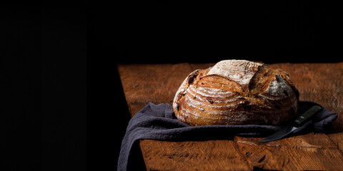 Rustic sourdough bread with cranberry on a wooden table. Panorama, black background with free space...