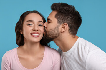 Obraz premium Man kissing his smiling girlfriend on light blue background