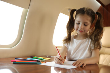 Cute little girl drawing at table in airplane during flight
