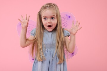 Cute little girl in fairy costume with violet wings on pink background