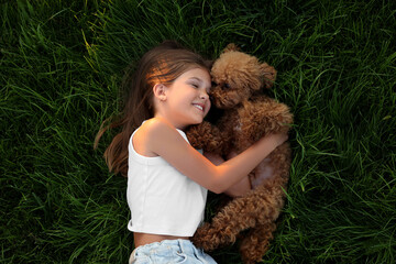 Beautiful girl with cute Maltipoo dog on green lawn outdoors, top view - Powered by Adobe