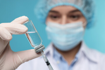 Doctor filling syringe with medication from glass vial on light blue background, selective focus