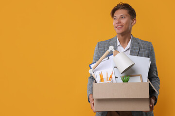 Happy unemployed young man with box of personal office belongings on orange background. Space for...