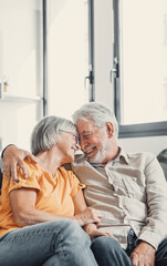 Happy laughing older married couple talking, laughing, standing in home interior together, hugging...