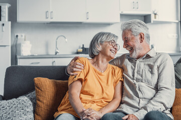 Happy mature husband and wife sit rest on couch at home hugging and cuddling, show care affection,...