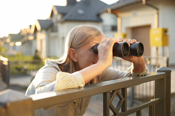Concept of private life. Curious senior woman with binoculars spying on neighbours over fence...