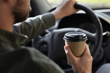Coffee to go. Man with paper cup of drink driving his car, closeup