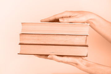 Stack of old books in hands on peach background, education, learning, study, compassion, connection.