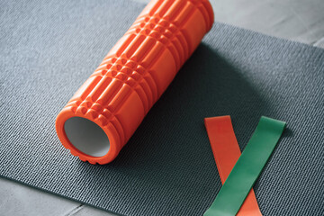 Close up view of yoga mat and orange colored foam roller for spine exercises