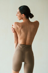 Back view, showing the spine, without bra. Young woman with slim body type is in fitness clothes in the studio