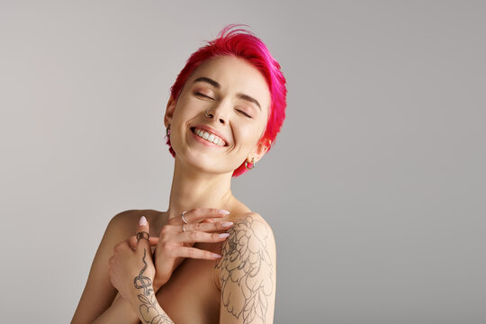 portrait of cheerful and topless young woman with bare shoulders and tattoo on grey background