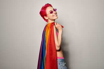 Fototapeta premium young and pleased female activist with pink hair and sunglasses posing with lgbt rainbow flag
