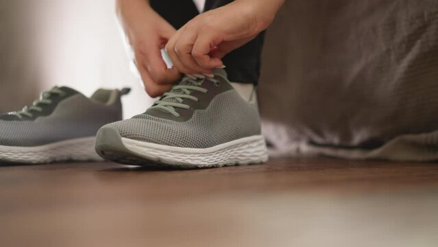 Woman adjusts sneaker tongue at home closeup. Sportswoman with shoes prepares for running in domestic gym slow motion. Active lifestyle