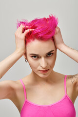 Naklejka premium portrait of alluring young woman with pink hair and tattoos posing and touching her hair, fashion