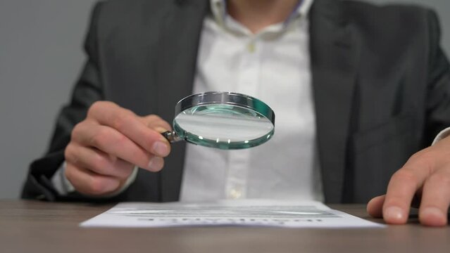 Embark on a journey of close inspection and detailed exploration with this captivating stock video capturing a man engrossed in examining a paper using a magnifying glass. The scene unfolds with a clo