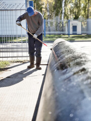 Man handyman paints large diameter metal pipe outside with paint roller on summer day. Protection of metal from corrosion.