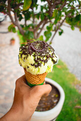 Imagen vertical de una mano sosteniendo un helado de cono con limón y chocolate  - obrazy, fototapety, plakaty
