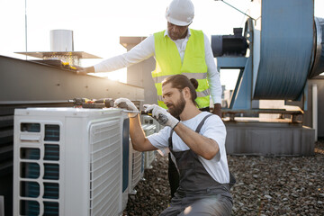 Skilled caucasian repairman fixing air conditioner with screwdriver while african american...