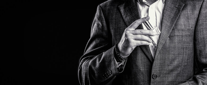 Fragrance smell. Men perfumes. Fashion cologne bottle. Man holding up bottle of perfume. Men perfume in the hand. Man in formal suit, bottle of perfume, closeup. Black and white