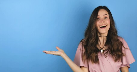 Excited surprised woman look at side, say wow and pointing hands aside isolated on blue background. Brunette girl in pink dress. Look over here. Sale here. Thumb up. - Powered by Adobe