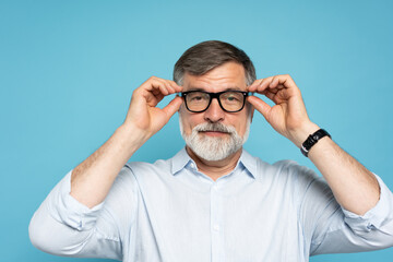 Happy caucasian mature man trying new glasses and smiling, standing on blue background