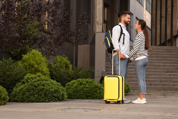 Long-distance relationship. Man with luggage holding hands with his girlfriend near building outdoors