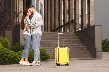 Long-distance relationship. Beautiful young couple kissing and suitcase near building outdoors