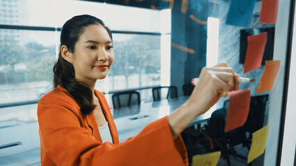 Portrait of young beautiful businesswoman writing marketing idea on glass board. Asian project...