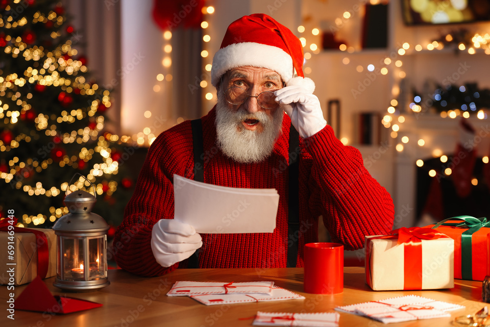 Canvas Prints Santa Claus reading letter at his workplace in room with Christmas tree