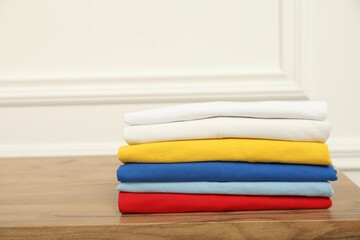 Sorting and organizing. Stack of different folded clothes on wooden table near white wall, space for text