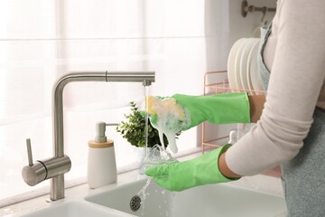 Woman washing glass at sink in kitchen, closeup