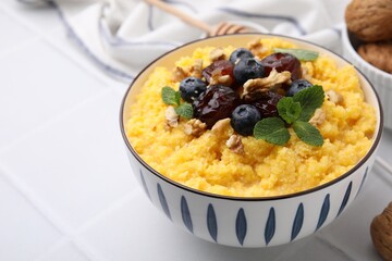 Tasty cornmeal with blueberries, dates, walnuts and mint in bowl on white table, closeup
