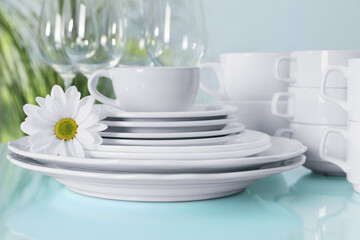 Set of clean dishware and flower on light blue table, closeup