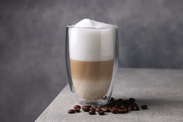 Aromatic latte macchiato in glass and coffee beans on light grey table