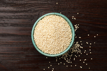 Dry quinoa seeds in bowl on wooden table, top view