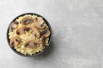 Delicious bulgur with mushrooms in bowl on gray table, top view. Space for text