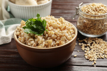Delicious pearl barley with parsley in bowl on wooden table, closeup