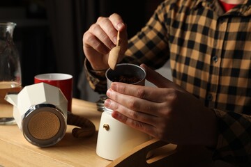 Man putting ground coffee into moka pot at table indoors, closeup