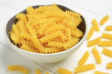 Raw fusilli pasta in bowl on white wooden table, closeup