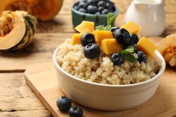 Tasty quinoa porridge with blueberries, pumpkin and mint in bowl on wooden table, closeup
